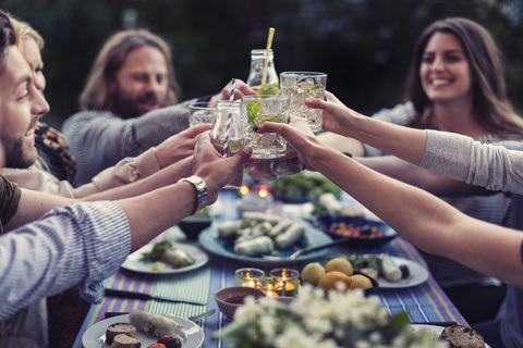 Happy friends toasting mojito glasses at dinner table in yard stock photo