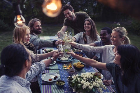 Happy multi-ethnic friends toasting drinks at dinner table in yard stock photo