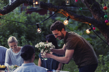Glücklicher Mann, der eine Blumenvase hält, während er eine Dinnerparty mit Freunden im Garten genießt - MASF04251
