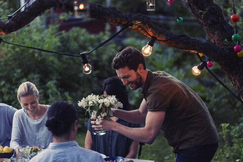 Glücklicher Mann, der eine Blumenvase hält, während er eine Dinnerparty mit Freunden im Garten genießt - MASF04251