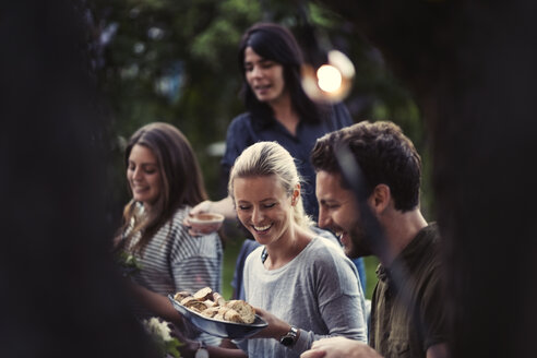 Glückliche Frau, die eine Brotschale hält, während sie ein Abendessen mit Freunden im Garten genießt - MASF04252