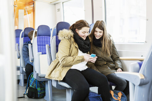 Glückliche junge Freundinnen benutzen ein Mobiltelefon während einer Zugfahrt - MASF04255
