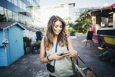 Happy female tourist using smart phone in city - MASF04257