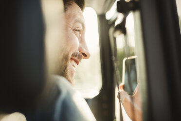 Glücklicher Mann schaut weg, während er mit seinem Smartphone im Auto fotografiert - MASF04268