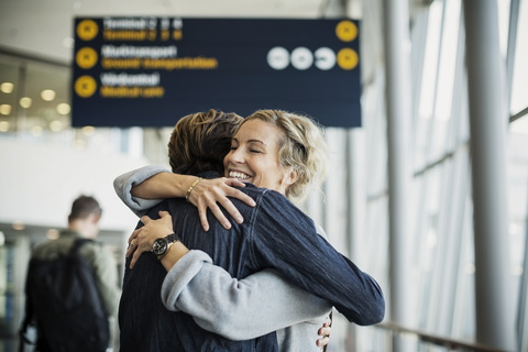Glückliche Geschäftsfrau umarmt männlichen Kollegen am Flughafen, lizenzfreies Stockfoto