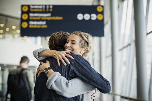 Glückliche Geschäftsfrau umarmt männlichen Kollegen am Flughafen - MASF04269