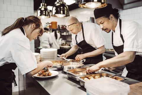 Kvinnlig sous chef och två manliga kockar förbereder maträtter, lizenzfreies Stockfoto