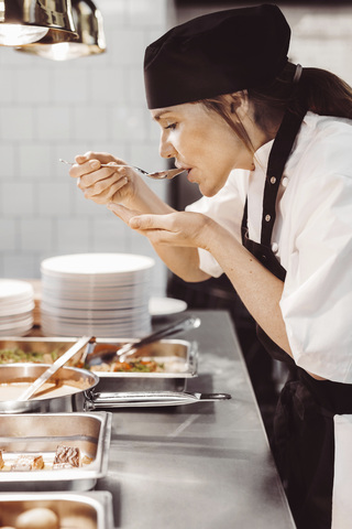 Kvinnlig kock smakar av i restaurangkök, lizenzfreies Stockfoto