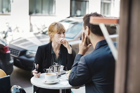 Männliche und weibliche Pendler sitzen in einem Straßencafé, lizenzfreies Stockfoto