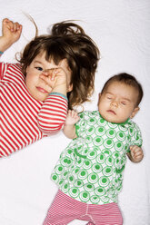 Hochwinkliges Porträt eines Mädchens, das sich die Augen reibt, während es neben einem schlafenden Baby im Bett liegt - MASF04290
