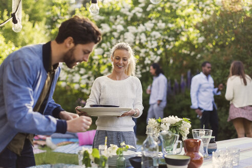 Glückliche junge Frau hält Teller, während sie ein Sommerfest mit Freunden im Garten genießt - MASF04315