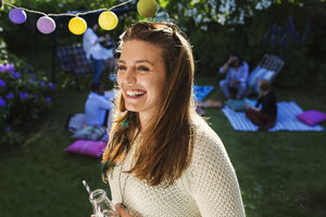 Glückliche junge Frau mit Freunden im Hintergrund auf dem Hof während eines Sommerfestes - MASF04316