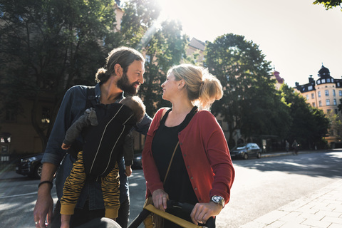 Loving mid adult parents with baby boy walking on sidewalk in city stock photo