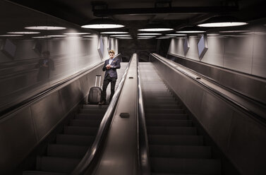 Low angle view of businessman with luggage checking time on escalator in airport - MASF04331