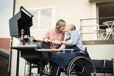 Disabled man in wheelchair kissing woman while barbecuing at yard - MASF04348