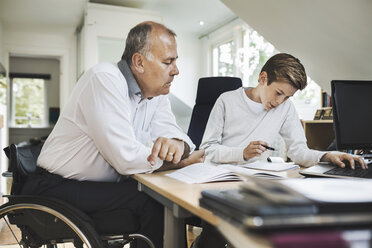 Disabled father assisting son in doing homework at home - MASF04349