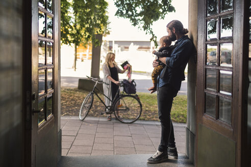 Vater an der Tür, der sein Baby hält, während er die Frau betrachtet, die zur Arbeit geht - MASF04379