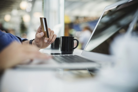 Ausgeschnittenes Bild eines Geschäftsmannes, der eine Kreditkarte und einen Laptop in der Flughafenhalle benutzt, lizenzfreies Stockfoto