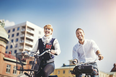 Happy business people riding bicycles in city against blue sky - MASF04393