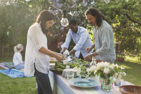 Friends preparing food at dining table in backyard during summer party - MASF04414