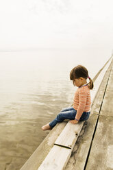 Full length side view of girl sitting on pier at beach - MASF04421