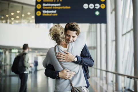 Glücklicher Geschäftsmann umarmt Kollegen am Flughafen, lizenzfreies Stockfoto