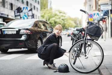Geschäftsfrau schaut weg, während sie ein Fahrrad auf der Straße repariert - MASF04438