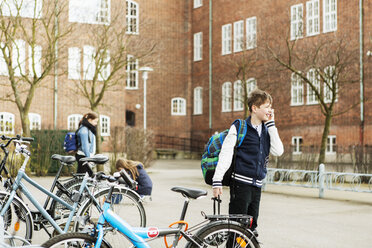 Boys talking on mobile phone by bicycle parking area outside school building - MASF04467