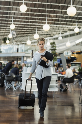 Geschäftsmann benutzt sein Smartphone beim Spaziergang am Flughafen, lizenzfreies Stockfoto