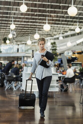 Businessman using smart phone while walking at airport - MASF04473