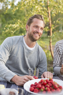 Smiling man having lunch with friend at picnic table - MASF04524