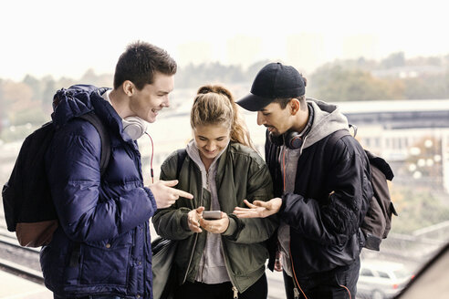 Lächelnde Freunde, die in einer U-Bahn-Station gemeinsam ein Mobiltelefon benutzen - MASF04525