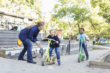 Teacher motivating children on push scooters during race - MASF04528