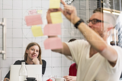 Young businessman writing ideas on adhesive notes with colleagues in background at creative office stock photo