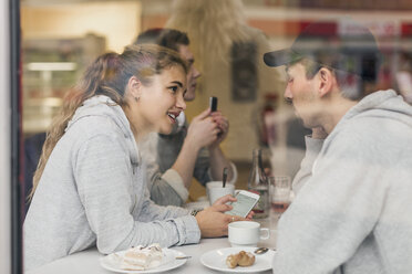 Blick auf ein junges Paar, das sich in einem Café über sein Smartphone unterhält, durch Glas - MASF04581