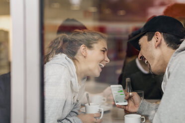 Blick auf ein glückliches junges Paar, das in einem Café ein Smartphone benutzt, durch Glas - MASF04584