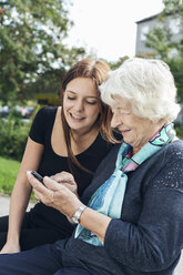 Junge Frau schaut Großmutter an, die im Park ein Smartphone benutzt - MASF04587
