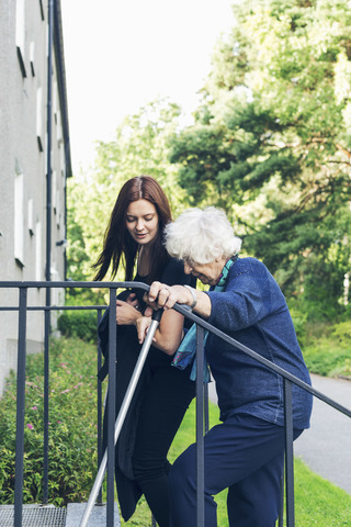 Junge Frau hilft ihrer Großmutter beim Treppensteigen im Freien, lizenzfreies Stockfoto
