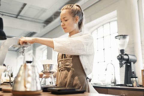 Junge Arbeiterin bereitet Kaffee am Tresen zu, lizenzfreies Stockfoto