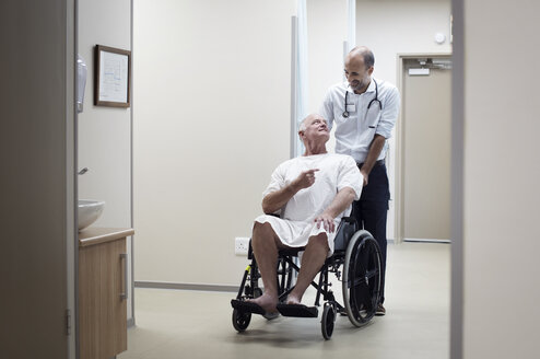 Arzt trägt Patientin auf Rollstuhl im Korridor - CAVF38467