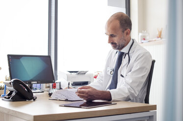 Arzt bei der Arbeit, während er am Tisch im Krankenhaus sitzt - CAVF38476