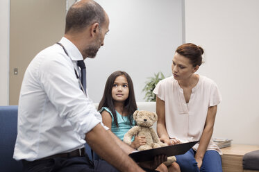 Mutter und Arzt sehen sich das Mädchen an, während sie auf dem Sofa im Krankenhaus sitzen - CAVF38494