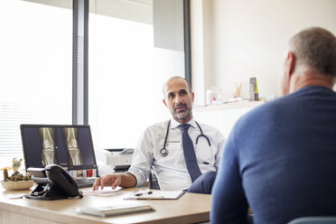 Doctor talking with patient while sitting at desk in hospital - CAVF38497