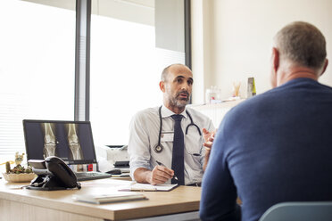 Doctor discussing with patient while sitting at desk in hospital - CAVF38498