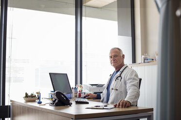 Porträt eines Arztes bei der Arbeit am Schreibtisch am Fenster im Krankenhaus - CAVF38507