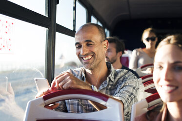 Glücklicher Mann, der ein Mobiltelefon benutzt, während er im Reisebus unterwegs ist - CAVF38527