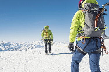 Rückansicht von Freunden mit Seil, die auf einem schneebedeckten Berg gegen einen klaren blauen Himmel laufen - CAVF38531