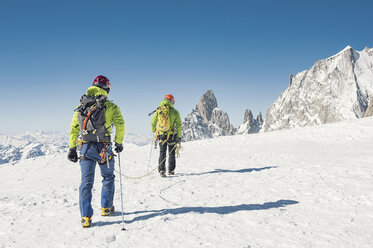 Rückansicht von Wanderern mit Seil, die auf einem schneebedeckten Berg gegen einen klaren blauen Himmel laufen - CAVF38532