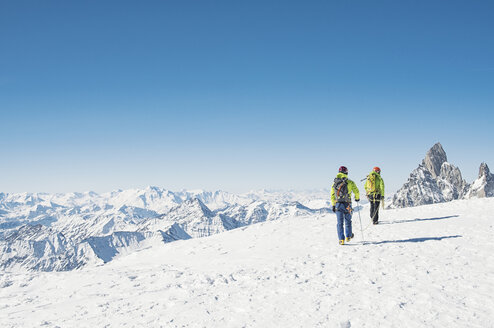 Rückansicht von Wanderern, die auf einem schneebedeckten Berg gegen einen klaren blauen Himmel wandern - CAVF38533
