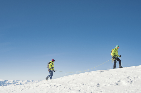 Seitenansicht von Wanderern, die auf einem schneebedeckten Berg gegen einen klaren blauen Himmel wandern, lizenzfreies Stockfoto